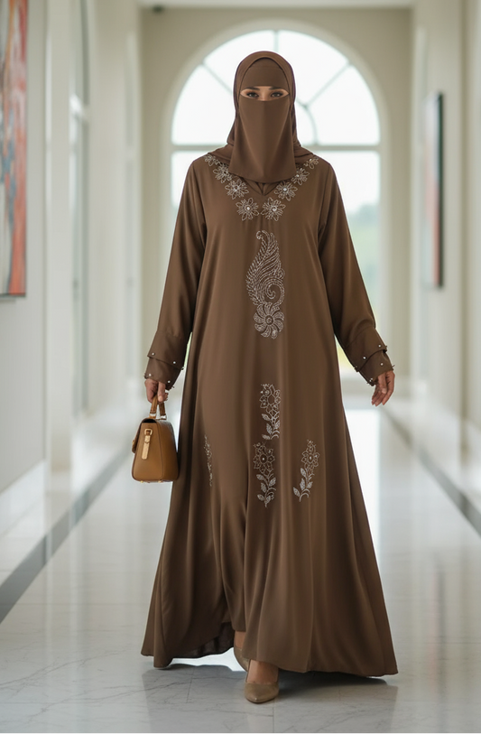 Woman in a brown embroidered abaya walking in a modern hallway.