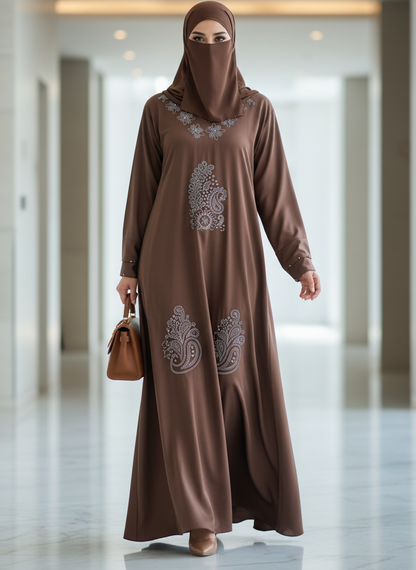 Woman wearing a brown abaya with intricate patterns in a modern building hallway.