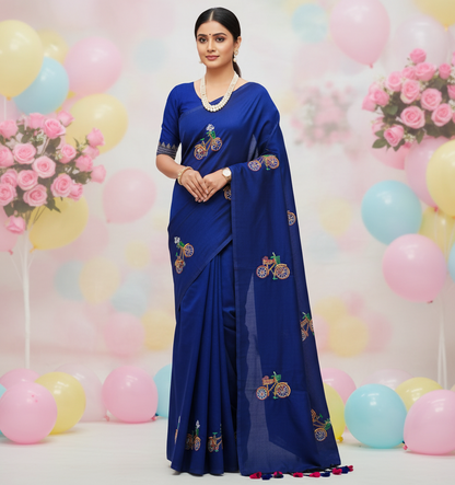 Woman in a blue saree with floral patterns against a colorful balloon and flower backdrop