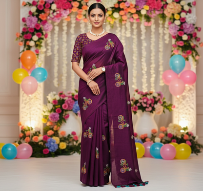 Woman in a purple saree with floral patterns standing in front of a decorated backdrop with flowers and balloons.